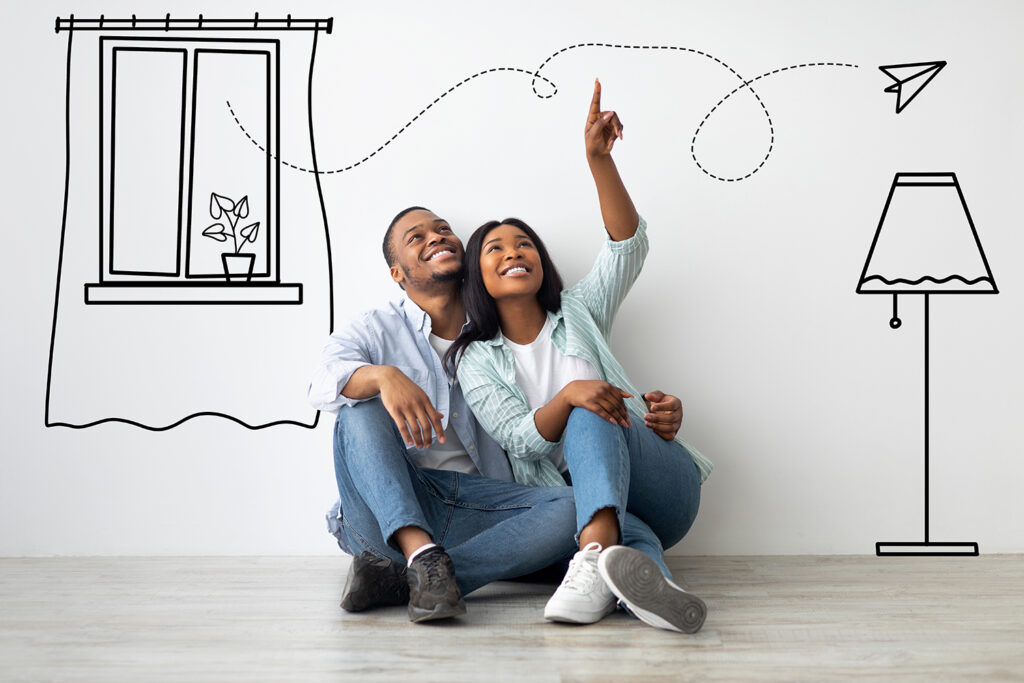 Loving african american couple imagining interior of their new flat, sitting on floor near white wall with doodle drawings